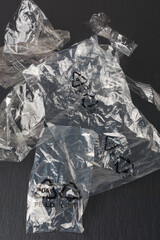 discarded recyclable clear plastic bags on textured black surface, thin and lightweight plastic or...