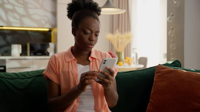 Confused unhappy sad ethnic African American business woman female girl businesswoman depressed client homeowner user holding mobile phone using app betting gambling fail lost loss money scam at home