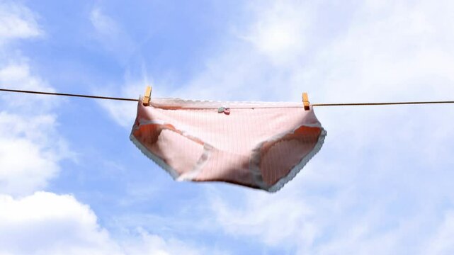 pink women's panties hang and dry on a clothesline on wooden clothespins and flutter in the wind against a background of blue sky with clouds, 4k video
