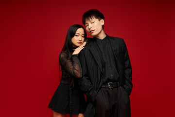 Stylish couple display love and confidence in fashionable outfits against a vibrant red backdrop