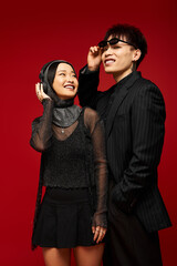 Stylish couple radiates love and joy against a vibrant red backdrop in modern fashion expressions