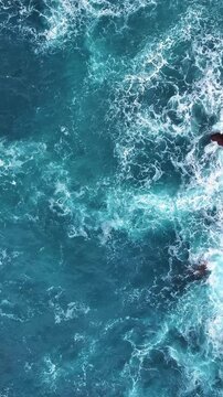 View of waves crashing against rocks in vibrant blue ocean. Vertical video