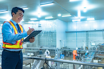Asian businessman and factory worker walks around inspecting factory and production line that uses machinery to handle and pack goods before export. Export tax and customs inspection by accountant.