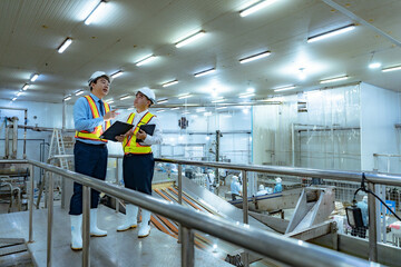 Asian businessman and factory worker walks around inspecting factory and production line that uses machinery to handle and pack goods before export. Export tax and customs inspection by accountant.