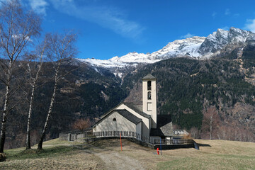 Catholic church in the Swiss Alps with mountains in the background in early spring