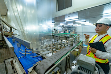 Asian factory workers are walking around inspecting the factory and production lines that use machinery to handle and pack goods before they are shipped out. Export