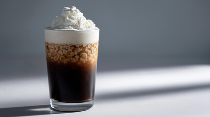 Iced coffee with whipped cream served in a clear glass under natural light on a minimalist background.
