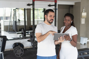 Personal trainer showing workout routine on tablet to client in gym