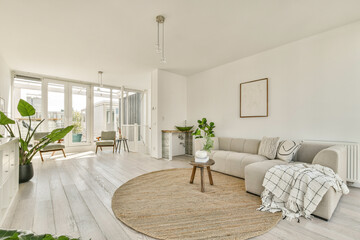 A bright, contemporary living room featuring a cozy sofa, decor plants, and large windows offering ample natural light, creating a warm and inviting atmosphere.