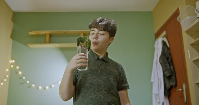 A young girl holds a glass of water for her pet green parrot to drink in her bedroom. The parrot perches on the glass and drinks. They enjoy their time together.