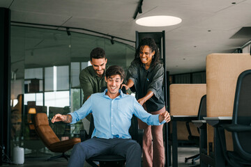Naklejka premium Young colleagues group having fun together riding on chairs in office diverse excited office workers