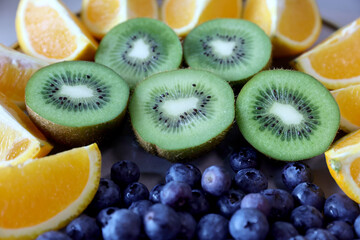 Fototapeta premium Closeup of colorful assorted fresh fruits, kiwi, bluerberryes and orange slices on a plate. Photographed in natural light.Selective focus.