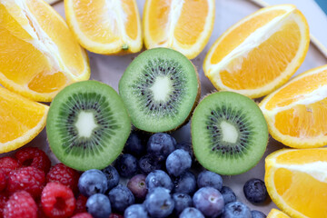Fototapeta premium Closeup of colorful assorted fresh fruits, kiwi, bluerberryes,red-raspberries and orange slices on a plate. Photographed in natural light.Selective focus.
