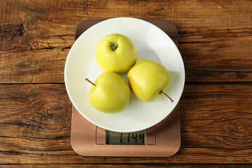 Modern electronic kitchen scale with apples on wooden table, top view