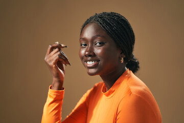 Young black woman smiling and touching her hair in studio with brown background