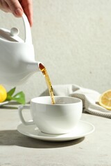 Woman pouring aromatic tea from teapot into cup at light textured table, closeup