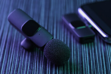 Lavalier microphone and smartphone with wireless receiver on dark wooden table in neon lights, closeup