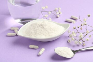 Collagen powder in bowl, spoon, pills, glass of water and gypsophila flowers on violet background, closeup