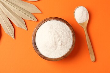 Collagen powder in bowl, spoon and dry palm leaf on orange background, flat lay