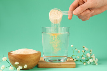 Woman adding collagen powder into glass with water on turquoise background, closeup