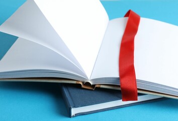 Book with red ribbon bookmark and hardcover one on light blue background, closeup