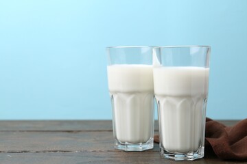 Fresh milk on wooden table against light blue background. Space for text