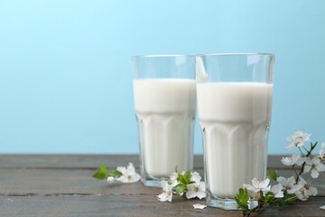Fresh milk and blossoms on white table against light blue background. Space for text