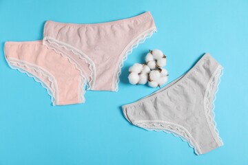 Women's underwear. Beautiful panties and cotton flowers on light blue background, flat lay