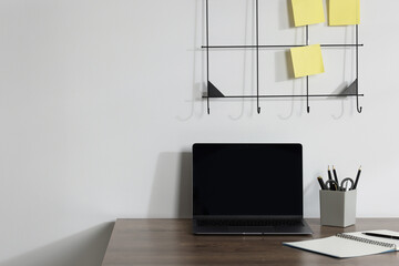 Laptop and different stationery on wooden office table near white wall, space for text