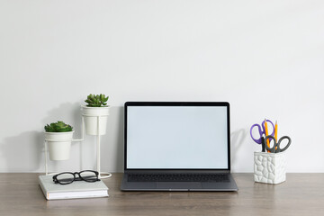 Laptop, different stationery, glasses and floral decor on wooden office table against white background