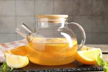 Glass teapot with aromatic fruit tea, orange, lemon and mint on table, closeup