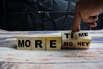 Concept word More time or more money, hand flip cubes and changes the inscription more money to more time on wooden blocks on a wooden table