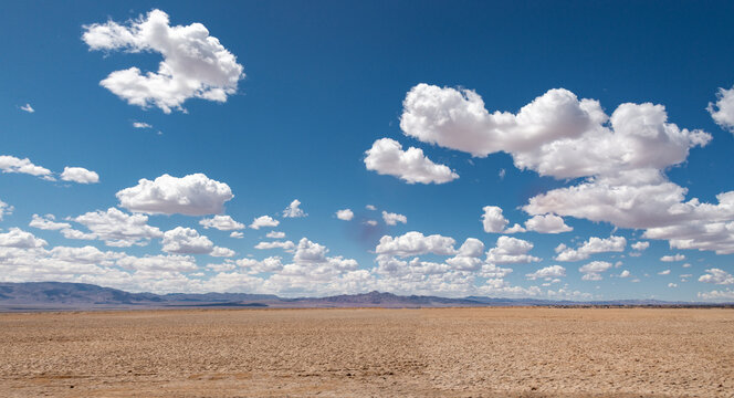 clouds over the field billowing fluffy cumulus desert sand dirt desolate isolated blue sky