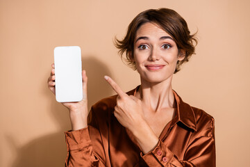 Photo of pretty shiny girl wear brown blouse pointing finger modern gadget empty space isolated beige color background
