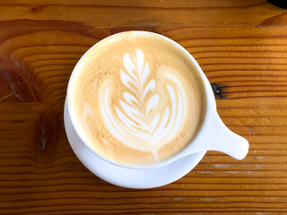 A white porcelain mug filled with an Italian chocolate latte, topped with white froth in the shape of a flower pattern. The top has brown chocolate dusting. The background is a yellowish wood table.