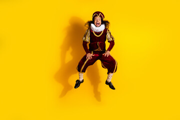 Portrait of a nobleman in historical costume jumping with enthusiasm against bright yellow studio...