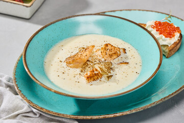 Creamy Fish Soup in Rustic Teal Bowl on Textured Surface with Vibrant Lighting