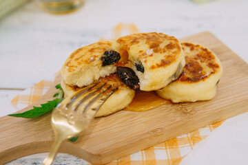 Cottage cheese pancakes with raisins and honey being taken with a golden fork served on a wooden board for breakfast snack food photography