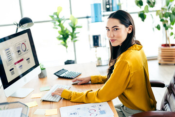 Skilled professional businesswoman working at a desk in a modern office with natural light and stylish decor, focusing on charts and data