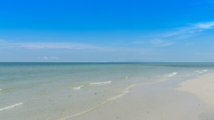 Serene coastal scene of clear bright blue sky meets a calm turquoise sea at the horizon. Foreground shows the sandy beach with gentle waves washing ashore.