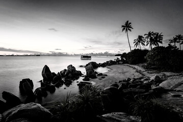 Black and white photo of a bridge over the sea at sunset.