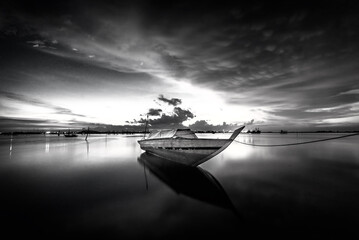Black and white photo of a bridge over the sea at sunset.