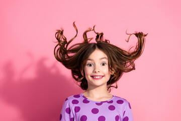 Happy young girl with wavy brown hair smiling cheerfully, wearing a trendy purple polka-dot top against a vibrant pink background