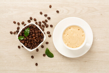 Cup of coffee with coffee beans and leaves on wooden background,top view