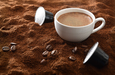 Espresso cup on ground coffee with capsules around elevated view