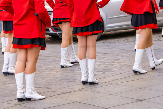 A group of majorettes in red uniforms and white boots performing in the street.