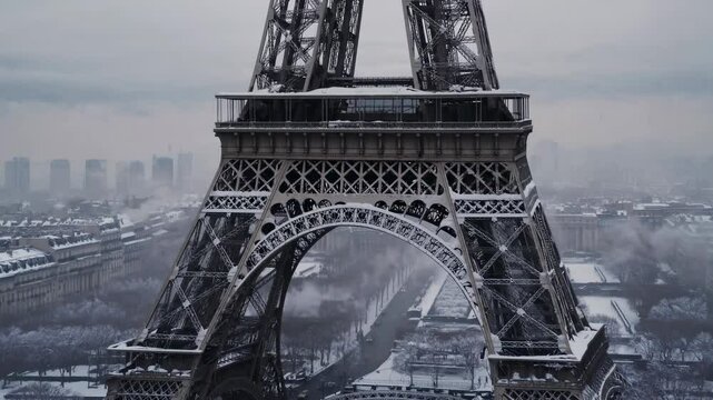 Aerial video captures the Eiffel Tower in winter, showcasing its snow-covered structure and the surrounding Parisian landscape from above.