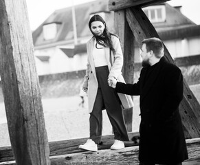 Caucasian couple holding hands walking on wooden structure outdoors in black and white