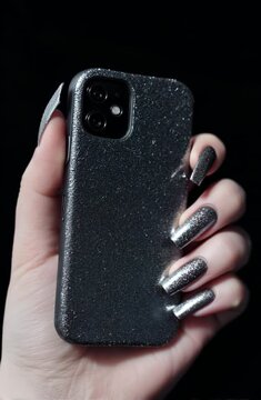 Woman holding and tilting a glittery phone case with a mirror-like finish, with metallic painted nails and a sleek black background.