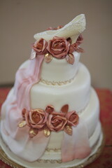 Elegant three-tiered wedding cake with pink roses and shoe topper